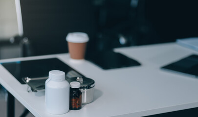 Female doctor writing in a notebook and holding a medicine bottle works at a computer while there were many medicine bottles on the table while sitting at a work desk