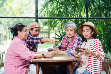 Elderly Asian women gathered around a wooden table in a bright cafe, engaging in a friendly discussion. One woman pointing while others listen attentively. Casual clothing, natural light,