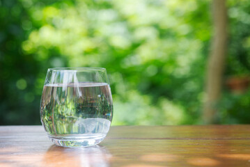 glass of drinking water on wooden table in in garden with green bokeh background.