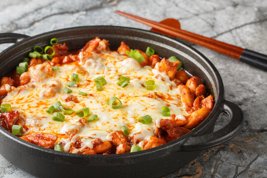 Korean Buldak Fire Chicken made of stir-fried spicy chicken that's been marinated in a variety of Korean spices covered with lots of mozzarella cheese closeup on the pan on the table. Horizontal