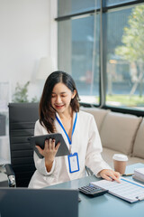 Young beautiful woman typing on tablet and laptop while sitting at the working white table