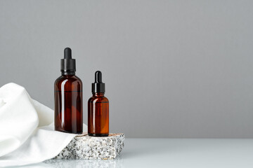 Set of brown glass bottles with essential oils on stand on gray background