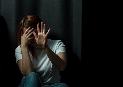 The woman in the photo looks depressed and scared, she has suffered from domestic violence or emotional abuse. Her posture is hunched, and her facial expression is anxious and sad