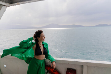 Woman wearing a green shirt and pants stands on the deck of a boat, looking out at a vast ocean....