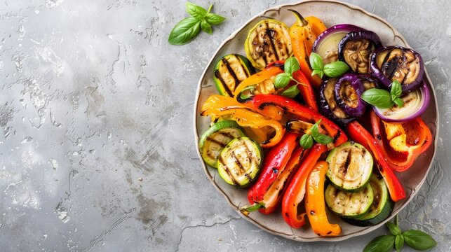 Colorful grilled vegetables including bell peppers, zucchini, and eggplant arranged on a plate placed on a light grey slate, stone, or concrete surface. Viewed from above with space for text