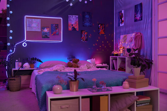 Background image of girls room interior with pink and purple neon lights over comfortable bed and fluorescent art copy space