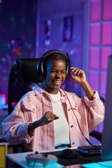 Vertical portrait of emotional Black young woman playing video games at night and celebrating victory with neon lighting © Mediaphotos