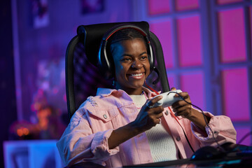 Portrait of smiling young African American woman playing video games and holding gamepad in studio with pink neon lights © Mediaphotos