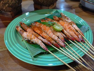 Grilled shrimp skewers served on a green plate with banana leaf garnish, showcasing a delightful and appetizing seafood dish