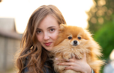 Beautiful young girl with a dog in her arms. Love to the animals. Pet on a walk. Animal protection. Pomeranian Spitz.