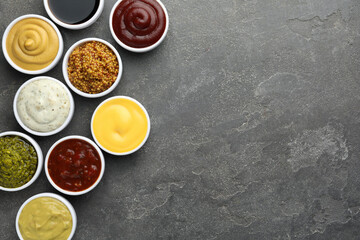 Many different sauces in bowls on grey table, top view. Space for text