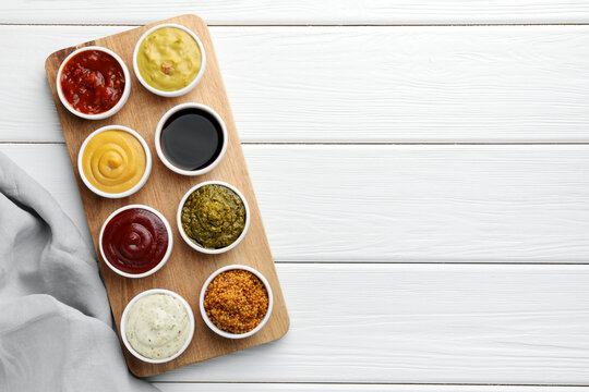 Many different sauces in bowls on white wooden table, top view. Space for text