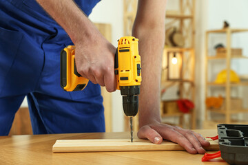 Craftsman working with drill at wooden table in workshop, closeup