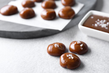 Tasty candies, caramel sauce and salt on light grey table