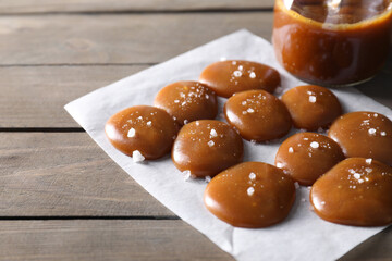 Tasty candies, caramel sauce and salt on wooden table, closeup