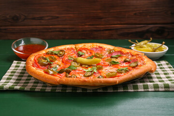 Delicious pizza Diablo, sauce and pickled peppers on green wooden table