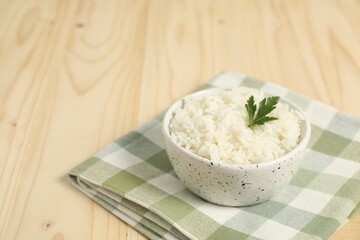 Delicious boiled rice in bowl and parsley on wooden table. Space for text