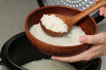 Woman taking boiled rice into bowl on grey background, closeup