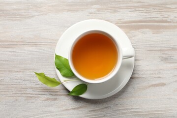 Refreshing green tea in cup and leaves on light wooden table, top view
