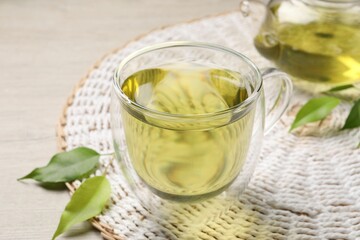 Refreshing green tea in cup, teapot and leaves on wooden table, closeup