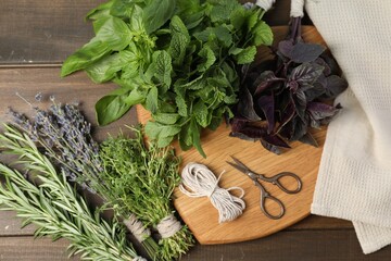 Different aromatic herbs, thread and scissors on wooden table, top view