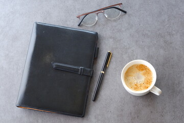 ミルクをたっぷり入れたコーヒー、カフェ・ラッテを飲みながら、システム手帳でデスクワーク中のイメージ
