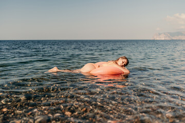 A woman is floating on a pink inflatable raft in the ocean. The water is calm and the sky is clear. The woman is enjoying her time in the water.