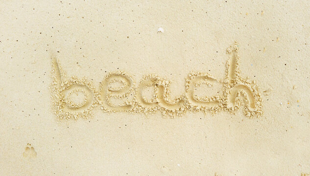 Writing in light yellowish sea sand of the word beach. Tropical island on clean sand with free areas for text. Photographed from above in close-up. Suitable for vacation postcards