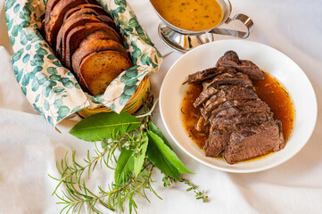 Baked venison loin, wild orange sauce, sliced toasted bread, bunch of herbs on white.
