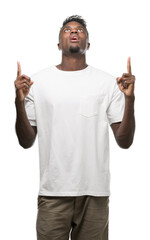 Fototapeta premium Young african american man wearing white t-shirt amazed and surprised looking up and pointing with fingers and raised arms.