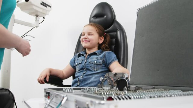 An optician checks the vision of a small child. A female doctor uses special glasses to diagnose a patient's eyes and select lenses in the clinic. Ophthalmology concept.