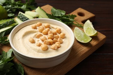 Tasty hummus with chickpeas in bowl and fresh products on wooden table, closeup