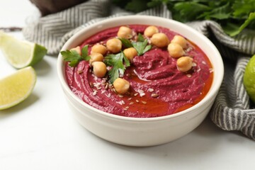Tasty beet hummus with chickpeas and parsley in bowl on white table, closeup