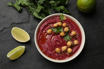 Tasty beet hummus with chickpeas in bowl, lime and parsley on grey textured table, flat lay