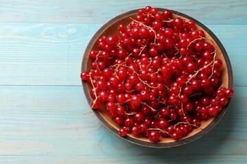 Fresh red currants in bowl on light blue wooden table, top view. Space for text