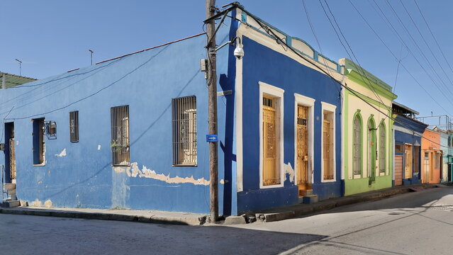 One-storey Colonial townhouses of blue-green-orange facades, wooden doors and grille windows, Clarin and Heredia Streets SW corner. Santiago-Cuba-514