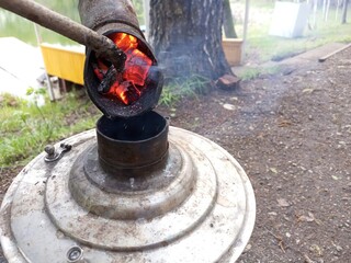 Lighting a camping samovar for making hot drinks like tea, coffee in nature near the lake by adding...
