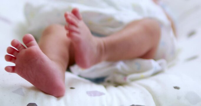 Close-up shot of a newborn baby stretching her left leg and then followed simultaneously by her right leg while she is lying on the bed.