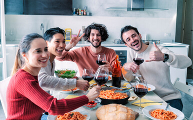 Happy ethnic group of friends eating pasta and drinking wine at home lunch party