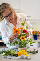 Woman arranging colorful flowers in a ceramic vase in a kitchen