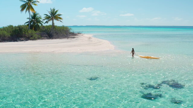 Woman on tropical beach pull out kayak from crystal clear water. Palm tree under clear blue sky. Small exotic island in French Polynesia.. Outdoor lifestyle travel summer holiday vacation active sport