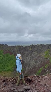 female tourist walks along edge of a Eldborg volcano crater in Iceland