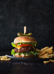 Close up of hamburger and french fries on wood with dark background.
