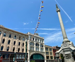 Monument with pride flag bunting & historic buildings in Troy, NY © Cavan