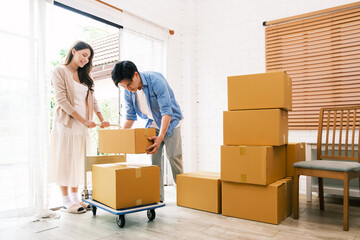 Asian young happy new married couple moving to their new house or real estate. An attractive romantic man and woman carry boxes parcel with happiness and love. Family moving house relocation concept.