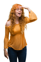 Young redhead woman very happy and smiling looking far away with hand over head. Searching concept.