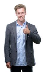 Young handsome blond business man doing happy thumbs up gesture with hand. Approving expression looking at the camera with showing success.