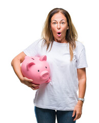 Middle age hispanic woman saving money using piggy bank over isolated background scared in shock...