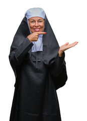 Middle age senior christian catholic nun woman over isolated background amazed and smiling to the camera while presenting with hand and pointing with finger.