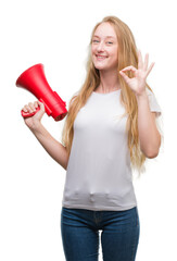 Blonde teenager woman holding megaphone doing ok sign with fingers, excellent symbol